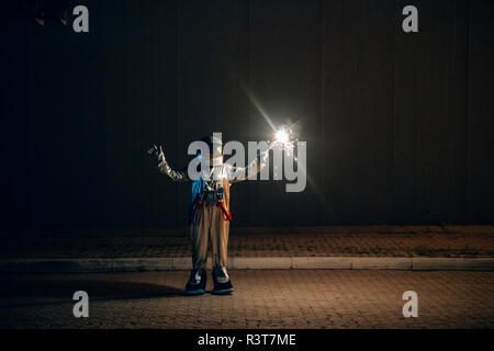 Spaceman in piedi su una strada di notte tenendo sparkler Foto Stock