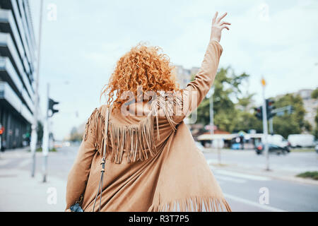 Redheaded donna salutando un taxi in strada Foto Stock