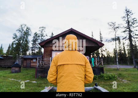 Uomo in piedi di fronte a log cabin, vista posteriore Foto Stock