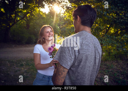 Giovane uomo incontro la sua fidanzata in un parco, gifting lei con fiori Foto Stock