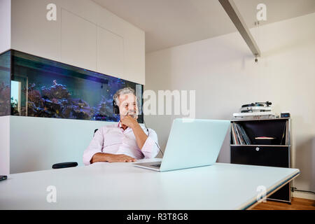 Imprenditore con cuffie utilizzando laptop al banco di fronte all acquario Foto Stock
