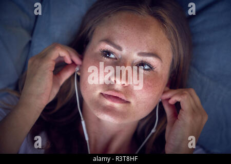 Giovane donna giaceva sul cuscino, ascoltando la musica con gli auricolari Foto Stock