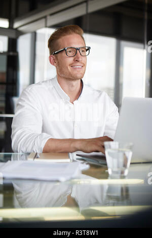 Imprenditore sorridente con notebook sulla scrivania in ufficio Foto Stock