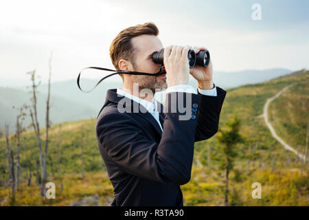 Imprenditore cerca attraverso il binocolo sulla cima di una montagna Foto Stock