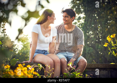 Romantico coppia giovane seduto sulla parete in un parco con bracci intorno Foto Stock