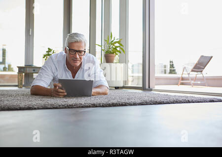 Uomo maturo giacente su un tappeto di casa utilizzando tablet Foto Stock