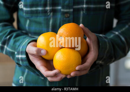 Uomo con le mani in mano regge quattro arance, close-up Foto Stock