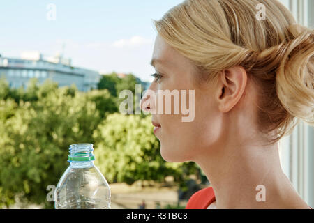 Giovane donna con bottiglia di acqua guardando fuori dalla finestra Foto Stock