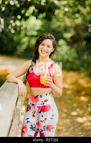 Giovane donna di bere succo di frutta dopo la pratica di Pilates in un parco urbano Foto Stock