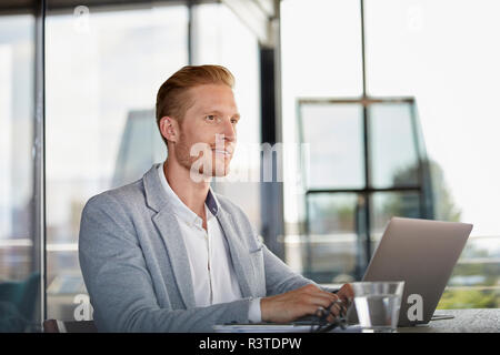 Imprenditore sorridente con notebook sulla scrivania in ufficio Foto Stock