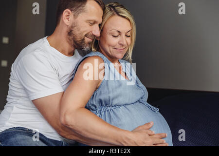 Uomo maturo e la sua gravidanza coppia moglie seduta sul letto di toccare la sua pancia Foto Stock