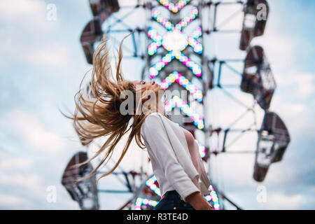 Con i capelli lunghi giovane donna scuotendo i suoi capelli su un luna park Foto Stock