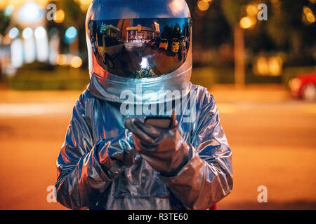 Spaceman su una strada della città di notte utilizza lo smartphone Foto Stock