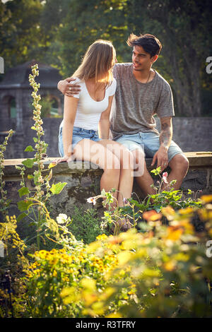 Romantico coppia giovane seduto sulla parete in un parco con bracci intorno Foto Stock