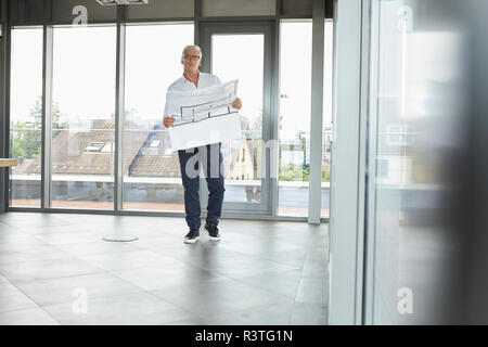 Imprenditore di successo in piedi in ufficio, tenendo il piano di costruzione Foto Stock