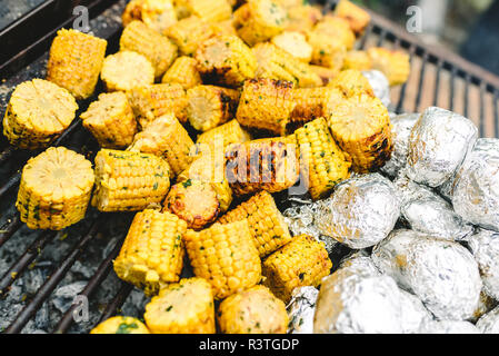 I tutoli di mais e patate avvolte in pellicola di alluminio su un barbecue. Foto Stock