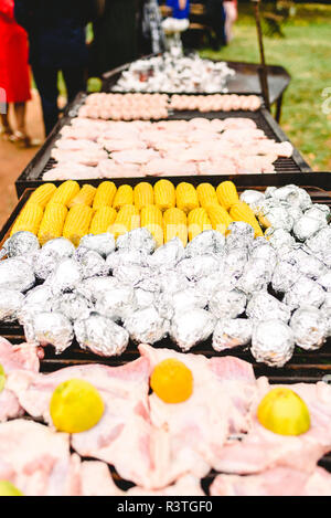 I tutoli di mais e patate avvolte in pellicola di alluminio su un barbecue. Foto Stock