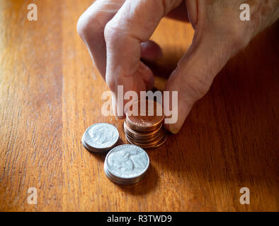 Una donna anziana monete di impilamento su un tavolo di legno. Solo le sue mani sono mostrati. Profondità di campo. Foto Stock