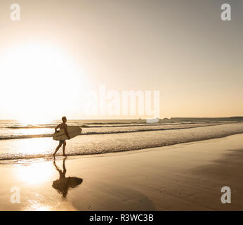 Giovane uomo che corre sulla spiaggia, portando le tavole da surf Foto Stock
