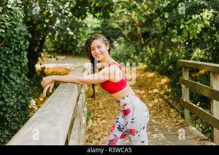 Giovane donna sorridente durante la pausa dopo la pratica di Pilates in un parco urbano Foto Stock