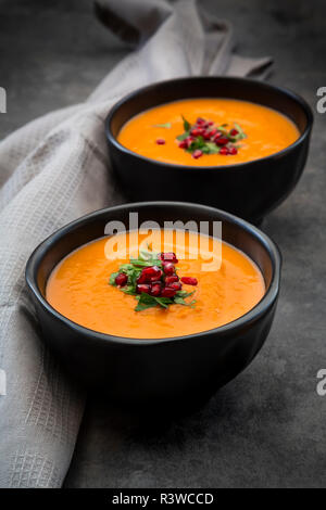 Tazza di Carote allo Zenzero Zuppa di cocco con topping di prezzemolo e semi di melograno Foto Stock