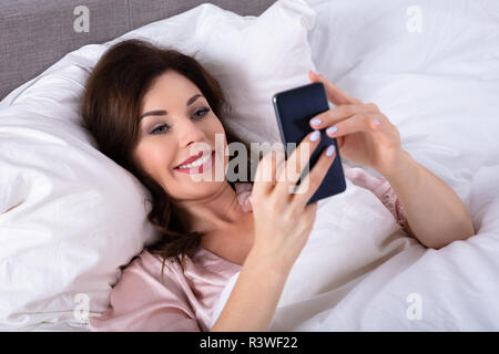 Felice giovane donna giaceva sul letto tramite cellulare Foto Stock