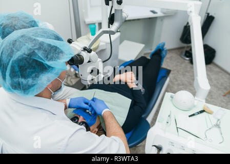 Medico ha utilizzato microscopio. Il dentista è di trattare il paziente in moderno studio dentistico. Il funzionamento è effettuata utilizzando camera stagna. Client è inserito e ripristinato Foto Stock