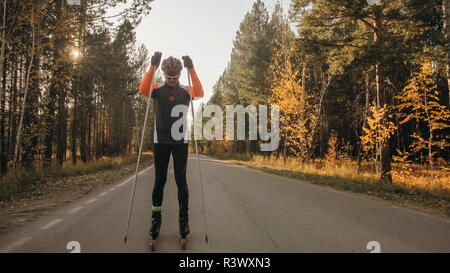 La formazione di un atleta sul rullo pattinatori. Il biathlon ride sul rullo di sci con bastoncini da sci, nel casco. Allenamento di autunno. Sport a rullo. Uomo adulto rid Foto Stock