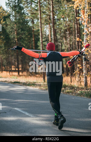 La formazione di un atleta sul rullo pattinatori. Il biathlon ride sul rullo di sci con bastoncini da sci, nel casco. Allenamento di autunno. Sport a rullo. Uomo adulto rid Foto Stock