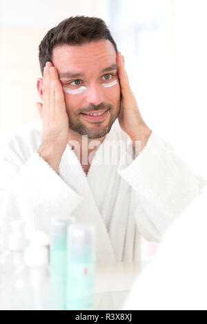 Giovane uomo attraente applicazione anti occhiaie crema attorno agli occhi Foto Stock