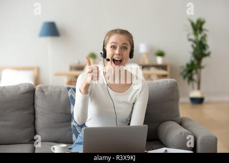 Ragazza eccitato in cuffia utilizzando laptop mostra pollice in alto Foto Stock