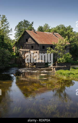 Abbandonato antico mulino ad acqua circondato da una splendida natura. Casa costruita in pietra e legno, muri esterni e fatiscente ponte sul fiume è reflecti Foto Stock