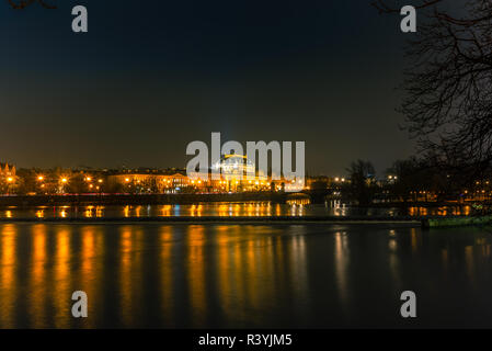 Illuminata edifici classici e le luci di strada riflettendo sul fiume Moldava a Praga prima di una piccola cascata in una fredda notte invernale - 1 Foto Stock