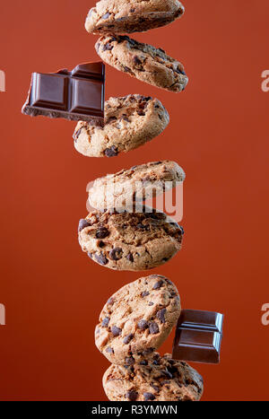 I biscotti al cioccolato e pezzetti di cioccolato in calo, sfondo marrone, levitazione alimentare Foto Stock