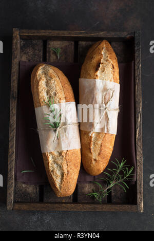 Freschi Fatti in casa il pane artigianale con rosmarino su sfondo rustico, vista dall'alto, copia dello spazio. Pasta madre mini baguette di pane. Foto Stock