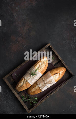 Freschi Fatti in casa il pane artigianale con rosmarino su sfondo rustico, vista dall'alto, copia dello spazio. Pasta madre mini baguette di pane. Foto Stock