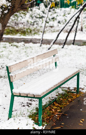 Prima neve sulla panchina nel parco della città in autunno Foto Stock