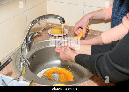 Close-up il lavaggio di stoviglie in quattro donne le mani in acciaio inox con lavello da cucina. Foto Stock