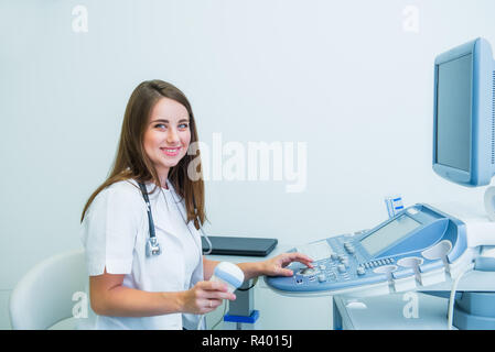 Ritratto di giovane medico sorridente, specialista di ultrasuoni guardando la fotocamera e mediante scansione a ultrasuoni Macchina per test pacient. Copia dello spazio. Selezione Foto Stock