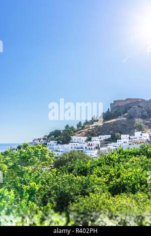 Foto verticale della famosa città di Lindos con tipiche case bianche. Acropolys è visibile al di sopra della città. Vista è sugli alberi verdi. Sky e blu chiaro è un Foto Stock