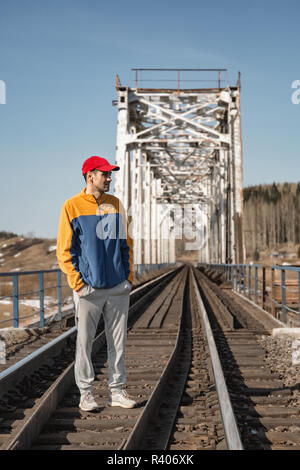 L uomo sta in una tuta in corrispondenza di un incrocio ferroviario sul ponte vicino - fino a primavera Foto Stock