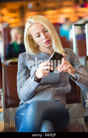 Viaggiatori femmina tramite telefono cellulare durante l'attesa. Foto Stock