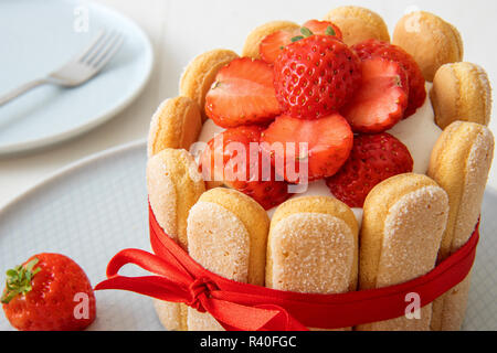 Malakoff Charlotte, dessert francese con fragole, legato con un nastro di scarlatto, tazza di caffè, ciotola con fragole su tavola bianca. Foto Stock