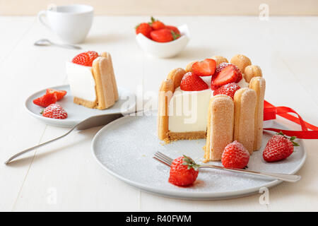 Charlotte, francese dessert con fragole, legato con un nastro rosso scarlatto, tazza di caffè, la ciotola con le fragole sul tavolo bianco. Non cuocere il dessert. Foto Stock