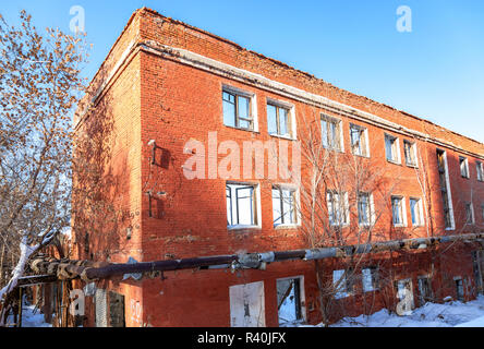 Vecchio e abbandonato edificio distrutto dal rosso mattone contro un cielo blu in giornata invernale Foto Stock
