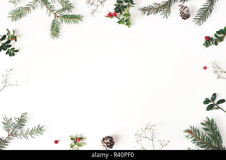 Natale cornice floreale, cornice decorativa. Composizione invernale di mirtillo rosso rami, bambino fiori di respiro, Abete rami di alberi e coni di larice sul tavolo bianco. Sfondo di festa. Appartamento laico, vista dall'alto. Foto Stock