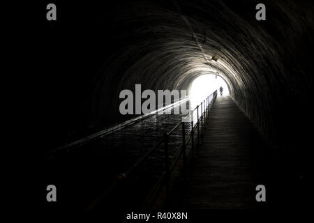 Silhouette di un uomo Appraching nella parte anteriore della luce alla fine del tunnel oscuro Foto Stock