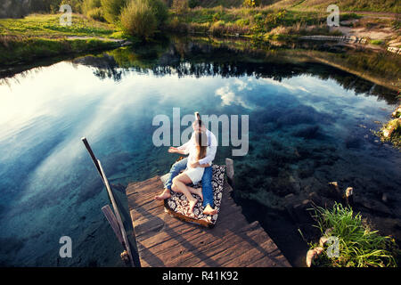 Gli amanti seduti sulla riva del fiume al tramonto Foto Stock