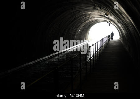 Silhouette di un uomo Appraching nella parte anteriore della luce alla fine del tunnel oscuro Foto Stock