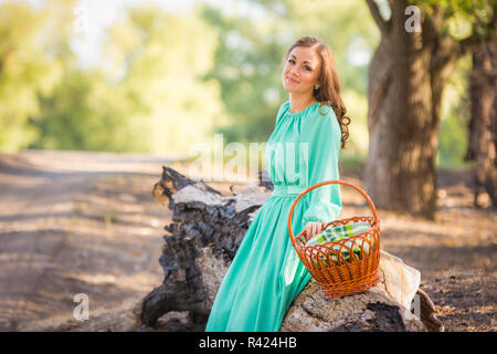 La ragazza con un cestello in una lunga veste sedette a riposare su un vecchio albero caduto Foto Stock